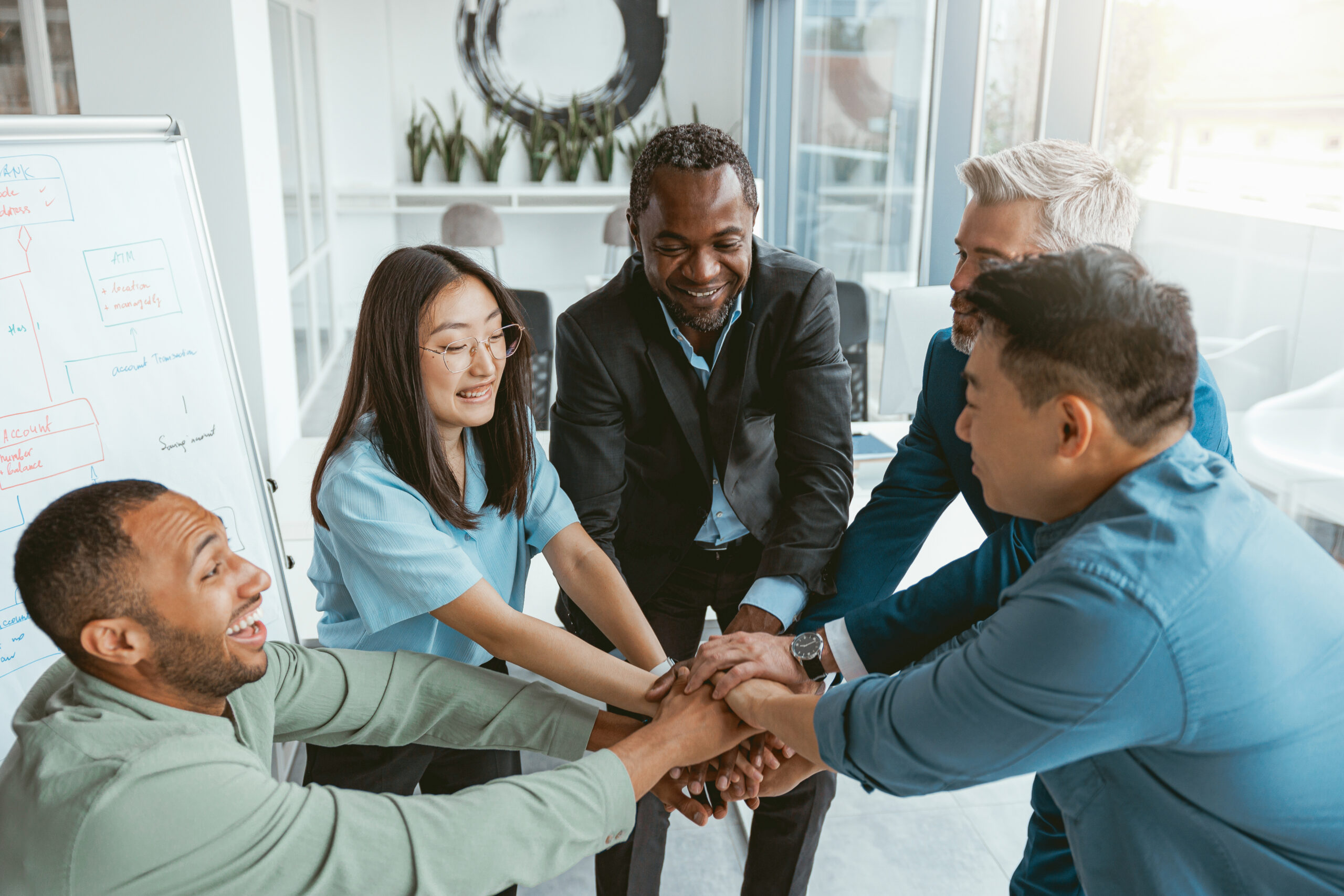 A multiracial team in a bright office with their hands stacked to showcase teamwork.